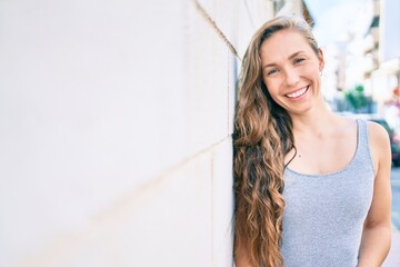 Young blonde woman smiling happy leaning on the wall at street of city