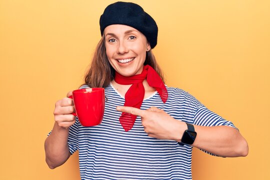 Young beautiful blonde woman wearing fashion beret drinking a cup of coffee smiling happy pointing with hand and finger