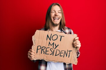 Handsome caucasian man with long hair holding not my president protest banner winking looking at...