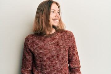 Handsome caucasian man with long hair wearing casual winter sweater looking to side, relax profile pose with natural face and confident smile.