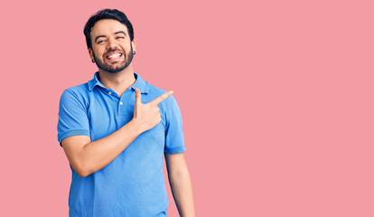 Fototapeta premium Young hispanic man wearing casual clothes cheerful with a smile of face pointing with hand and finger up to the side with happy and natural expression on face