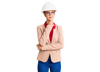 Young beautiful woman wearing architect hardhat serious face thinking about question with hand on chin, thoughtful about confusing idea