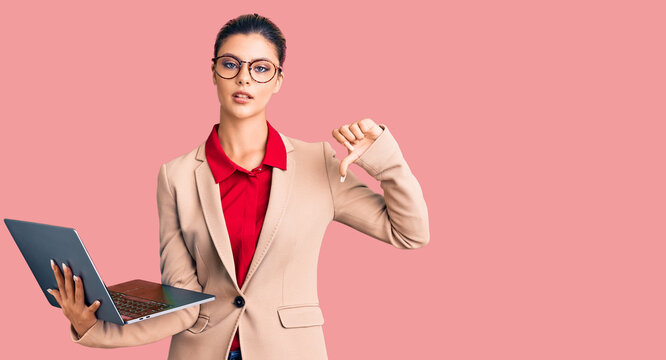 Young beautiful woman holding laptop with angry face, negative sign showing dislike with thumbs down, rejection concept