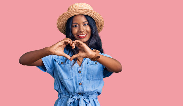 Young indian girl wearing summer hat smiling in love doing heart symbol shape with hands. romantic concept.