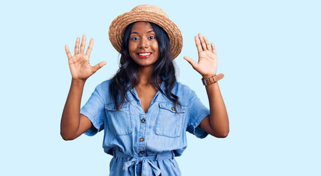 Young indian girl wearing summer hat showing and pointing up with fingers number ten while smiling confident and happy.