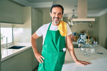 Middle age housekeeping man with beard smiling happy standing at the kitchen