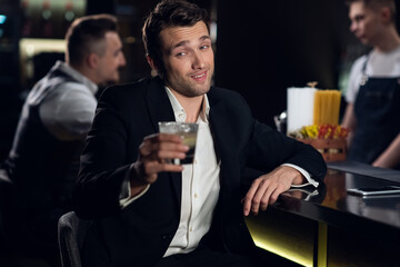 a beautiful man poses for a photo at the bar of a restaurant with a cocktail in his hands, portrait.