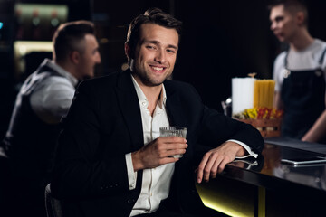 a beautiful man poses for a photo at the bar of a restaurant with a cocktail in his hands, portrait.