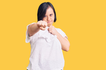 Brunette woman with down syndrome wearing casual white tshirt punching fist to fight, aggressive...