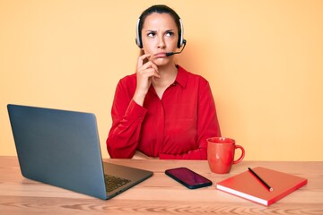 Young brunette woman wearing operator headset at the call center office serious face thinking about...