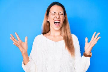 Young brunette woman wearing casual sweater crazy and mad shouting and yelling with aggressive expression and arms raised. frustration concept.