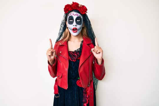 Woman wearing day of the dead costume over white amazed and surprised looking up and pointing with fingers and raised arms.