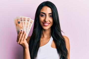 Beautiful hispanic woman holding united kingdom 10 pounds looking positive and happy standing and smiling with a confident smile showing teeth