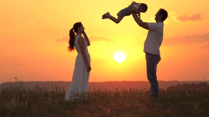 dad plays with his little daughter, happy to throw child into air, happy mom admires her family. mommy daddy and baby, family is resting at sunset in field. happy healthy family walking in fresh air.