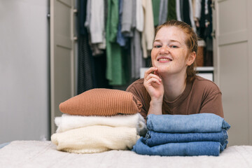 Woman folds in a stack of sweaters and jeans. Cleaning out wardrobe, clothes placed on hangers and in drawers