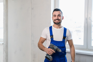 Man in blue overalls posing with a drill and smiling