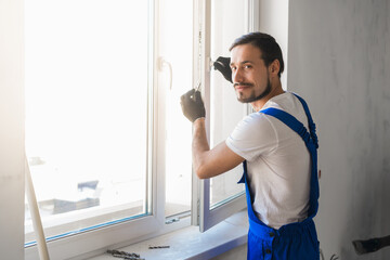 Male worker in overalls installs a window and poses at the camera
