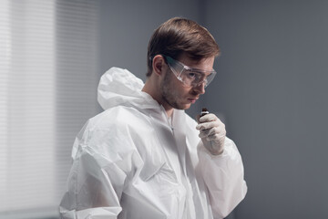 A clinician studying a new substance in the laboratory, cautiously sniffing a chemical reagent, isolated on white.