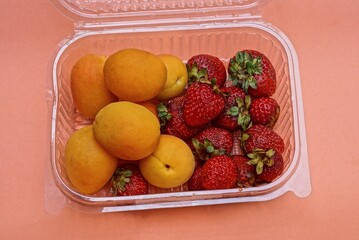 fresh and ripe strawberry and apricot fruits in a plastic box on an orange table