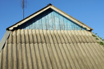 attic of a rural wooden house with a gray slate roof against a blue sky