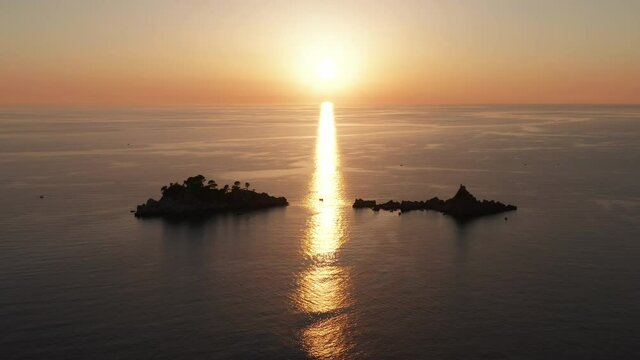 Silhouettes of two islands at golden sunset. Yellow sun in orange sky low above horizon and reflected in sea. Lonely tropical islets in the middle of the ocean. Vacation in paradise.
