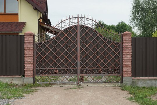 brown metal gate with forged pattern and part of a brick fence on the street