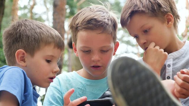 Boy with freckles on the face look at mobile. Children, brothers siblings looking at mobile. Three boys playing video game. Boys with gadget. Faces of three boys with phone outdoor. Leisure activity.