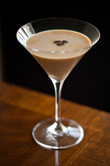 Creamy, tan espresso martini with floating coffee beans, single glass