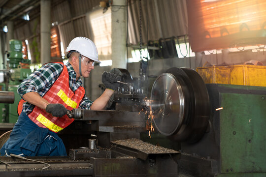 Male worker working on a lathe machine in metal industry factory on a business day. Professional engineer wearing a hard hat and safety glasses operating CNC milling machine in manufacturing workshop