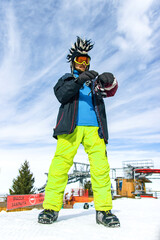 Attractive youg man tourist in funny mohawk hat, green pants, ski glasses mask and black mittens on...