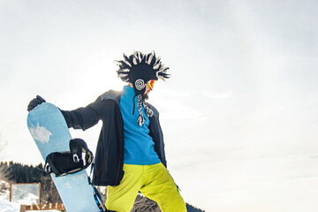 Snowboarder freerider in funny hat in the mountains is preparing to descend on the background of...