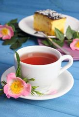 Cup of tea with cheesecake and wild rose flower on blue boards