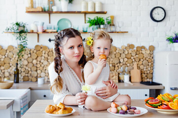Family portrait of a happy mother and daughter posing in the kitchen during Breakfast, eating delicious macaroons, cakes, cookies.