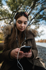 A caucasian woman using headphones and texting with her smartphone at park