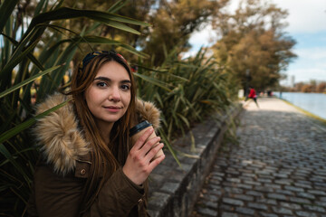 A pretty woman smiling at camera while relaxing at park and drinking a coffee. Vertical