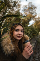 A pretty woman smiling at camera while relaxing at park and drinking a coffee. Vertical