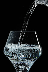 Mineral water is poured into a glass. Black background.