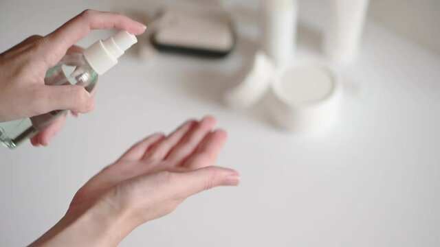 Woman at the white table with cosmetics set splashes hand lotion. Cosmetic product for hand skincare. Alcohol solution in transparent bottle with dispenser. Cleansing beauty product. Slow motion