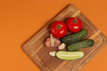 Sliced cucumber, tomatoes and garlic on wooden cutting board. Tomatoes with green ponytails. Healthy food. Copy space. High quality close-up photo