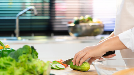 young Asian woman is preparing healthy food vegetable salad by Cutting cucumber for ingredients on cutting board on light kitchen, Cooking At Home and healthy food concept.