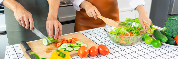Happy couple having fun standing in kitchen at home preparing vegetable salad husband and wife vegetarians chop vegetables prepare for dinner in loft kitchen at home.