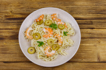 Spaghetti pasta with prawns, green olives and parsley on wooden table. Top view