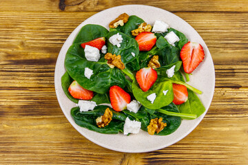 Fresh healthy salad with strawberry, spinach, walnuts and feta cheese on wooden table. Top view