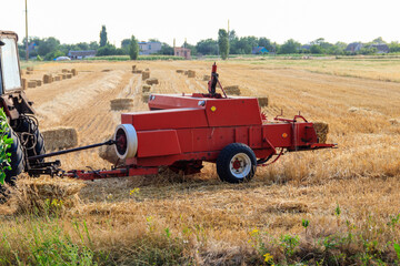 Fototapeta premium Rectangular baler discharges a straw bale in a field during the harvesting process