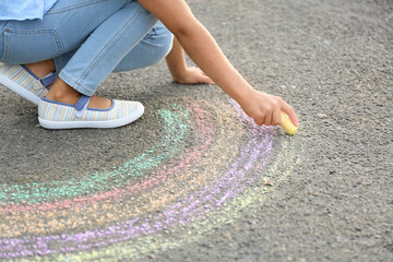 Little girl drawing rainbow with chalk on asphalt
