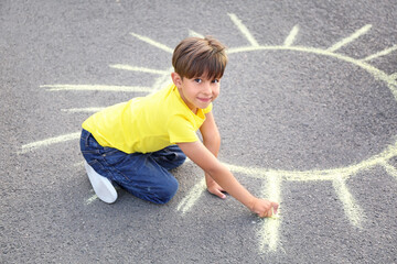 Little boy drawing sun with chalk on asphalt