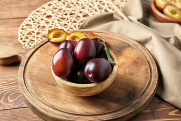Bowl with tasty sweet plums on table