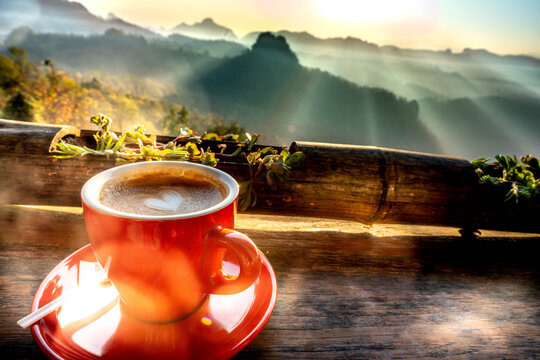 Latte art coffee cup with heart shape on wooden table monring fog and mist with mountain landscape view background.