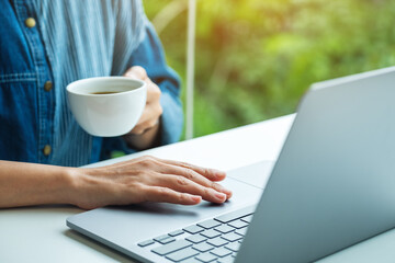 Closeup image of a woman working and touching on laptop computer touchpad while drinking coffee