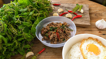 Stir fried pork with basil and chili  and fried egg with rice on wooden table